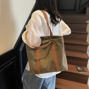 Grand sac fourre-tout en toile vert olive avec anses brunes sur un escalier en bois