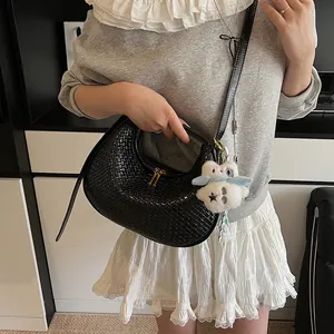 Detail of black woven crescent bag with golden double zipper and plush charm