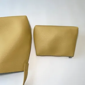 Detail view of mustard yellow pebbled leather tote bag set with metal zipper pouch