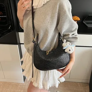 Detail of black woven crescent bag featuring gold zipper and plush doll pendant detail