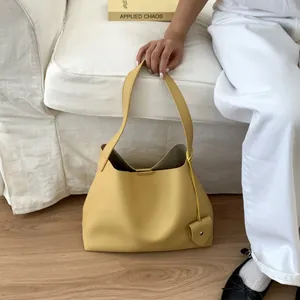 Detail of a bright yellow textured leather tote bag with a heart charm on a sofa