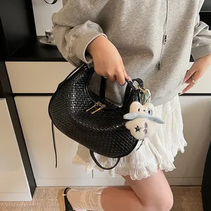 Close-up of black woven crescent bag with golden zipper and white plush rabbit charm