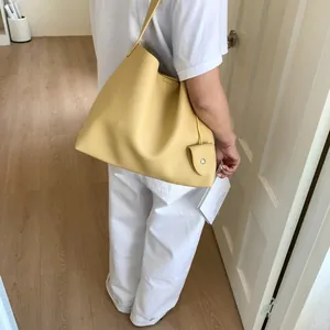 Close-up of a large yellow lychee textured leather tote bag worn by a model in a room