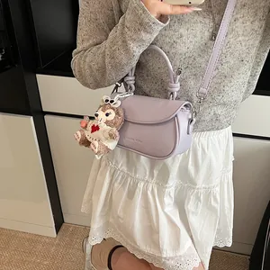 Détail du sac bandoulière lilas en similicuir avec logo et breloque ours en peluche