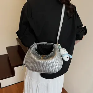 Detail showing silver woven texture on a crescent shoulder bag with plush charm