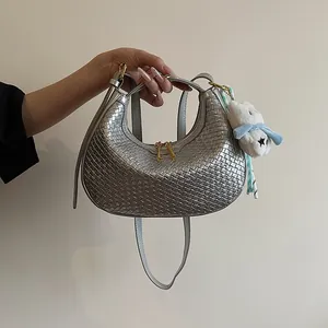 Close-up of metallic silver woven hobo bag featuring a white plush toy and dual zippers