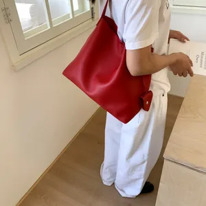 Detail of red lychee leather tote bag with heart charm shown on a female model