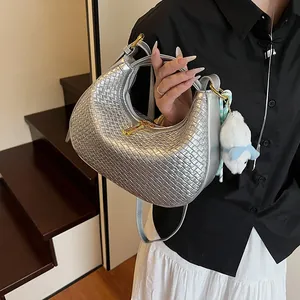 Close-up of silver woven hobo bag with a plush charm on a modern indoor staircase