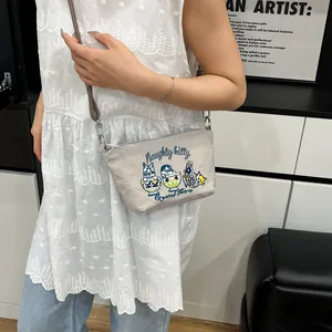 Close-up of beige crossbody bag with three cartoon cats and Naughty Kitty embroidery