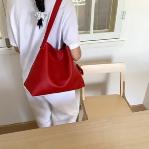 Red pebbled leather tote bag with wide strap shown on model in a cozy interior