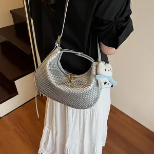 Detailed shot of a silver woven crescent hobo bag featuring a cute white plush dog charm