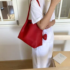 Detail of red litchi leather tote bag with long shoulder strap and heart charm