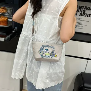 Detail of light gray crossbody bag featuring cute cat embroidery and adjustable strap