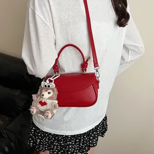 Détail du sac bandoulière en cuir rouge avec poignée nouée et charm ours en peluche