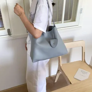 Blue-grey pebble grain leather tote bag worn by a model in a bright lifestyle setting