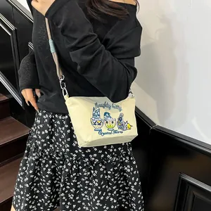 Detail showing blue cat embroidery and naughty kitty text on beige canvas crossbody bag