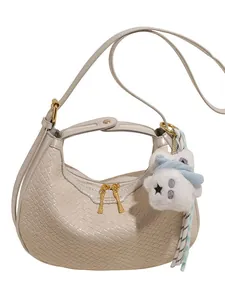 Beige crescent hobo bag with woven texture, golden zippers and plush bear charm