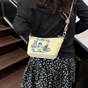 Detail of cute cat embroidery and knot shoulder strap on beige canvas crossbody bag