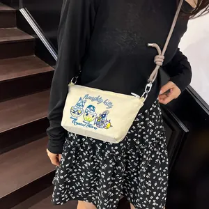 Detail of embroidered cartoon cats and Naughty kitty text on beige canvas crossbody bag