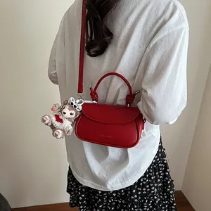 Détail du sac bandoulière rouge avec poignée nouée et breloque ours sur un mannequin