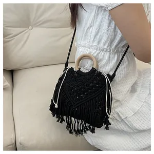 Detail of black woven bohemian handbag with fringe, wooden handles, and drawstring closure