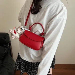 Détail du sac rouge à bandoulière avec poignée nouée et breloque ours en peluche sur le côté