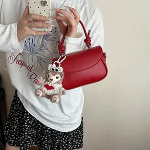 Détail du sac rouge à bandoulière avec poignée nouée, texture cuir et charme en peluche