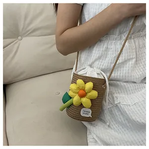 Dettaglio borsa a secchiello in paglia intrecciata con girasole e ciondolo floreale