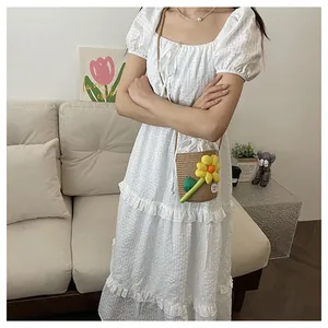 Dettaglio della borsa a secchiello in paglia floreale con coulisse su abito bianco