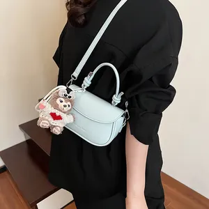 Gros plan du sac bandoulière bleu clair avec poignée supérieure et pendentif ours en peluche