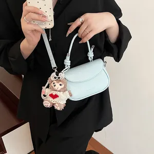 Détail du sac à bandoulière bleu clair avec breloque ours en peluche et poignée en cuir