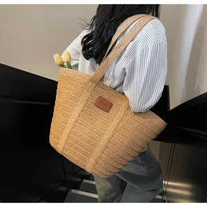 Détail du sac cabas en paille tressée avec écusson logo en cuir brun et décoration de tulipe