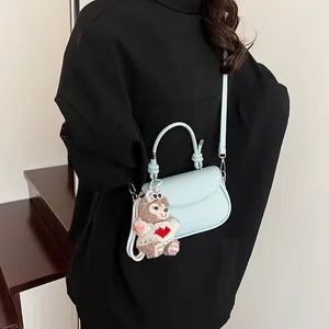 Détail du sac à bandoulière bleu clair avec breloque ours sur une tenue sombre