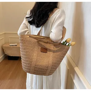 Détail d'un grand sac cabas en paille beige avec un écusson logo en cuir marron