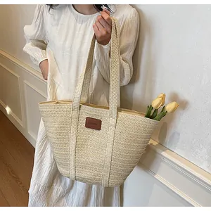 Détail du sac cabas en paille tissée avec écusson en cuir marron sur modèle en robe