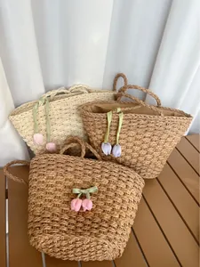 Trois sacs en paille avec pendentifs tulipe posés sur une table en bois rustique