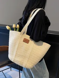 Grand sac cabas en paille tissée beige avec étiquette en cuir porté par un mannequin chic