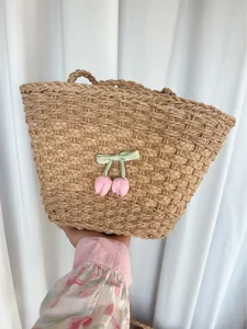 Détail du sac en paille tissé avec nœud vert et breloques cerises à carreaux roses