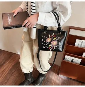 Gros plan sur un sac seau noir avec broderies florales délicates et anse en cuir