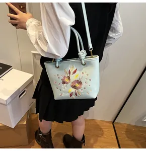 Détail de broderie avec paillettes et motifs floraux sur un sac seau en cuir bleu clair