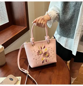 Détail du sac seau rose brodé avec motifs floraux sur une table en bois élégante