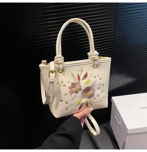 Détail de la broderie florale et des finitions dorées sur un sac seau beige