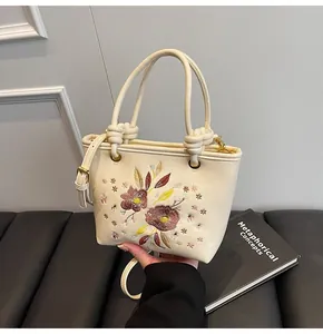 Détails de broderie florale et poignée nouée sur le sac seau en cuir de couleur crème