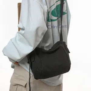 Close-up of black canvas messenger bag on model showing strap and side pocket detail