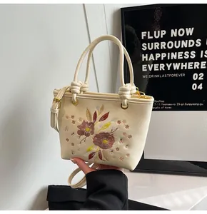 Détail de broderie florale sur un sac seau crème avec ferrures dorées et bandoulière