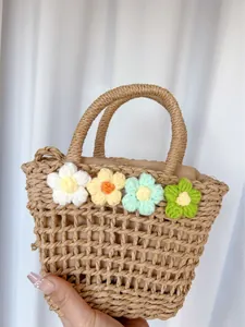 Detail of hand-woven straw bag featuring colorful 3D crochet flowers and sturdy handles