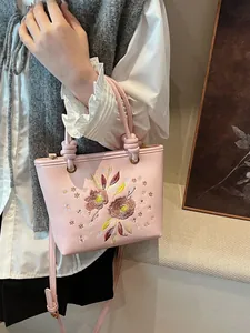 Sac seau rose avec broderie florale et bandoulière réglable, présenté sur un mannequin