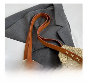 Détail de la bandoulière en similicuir marron avec coutures en X sur un sac en paille