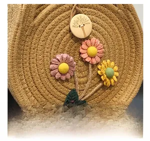 Détail du sac rond en paille montrant des marguerites en tissu et un bouton en bois