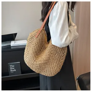 Détail de la texture tissée ajourée et de la bandoulière en cuir marron du sac de paille